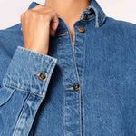 Close-up of a person wearing a blue denim shirt with buttoned sleeves.