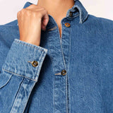 Close-up of a person wearing a blue denim shirt with buttoned sleeves.
