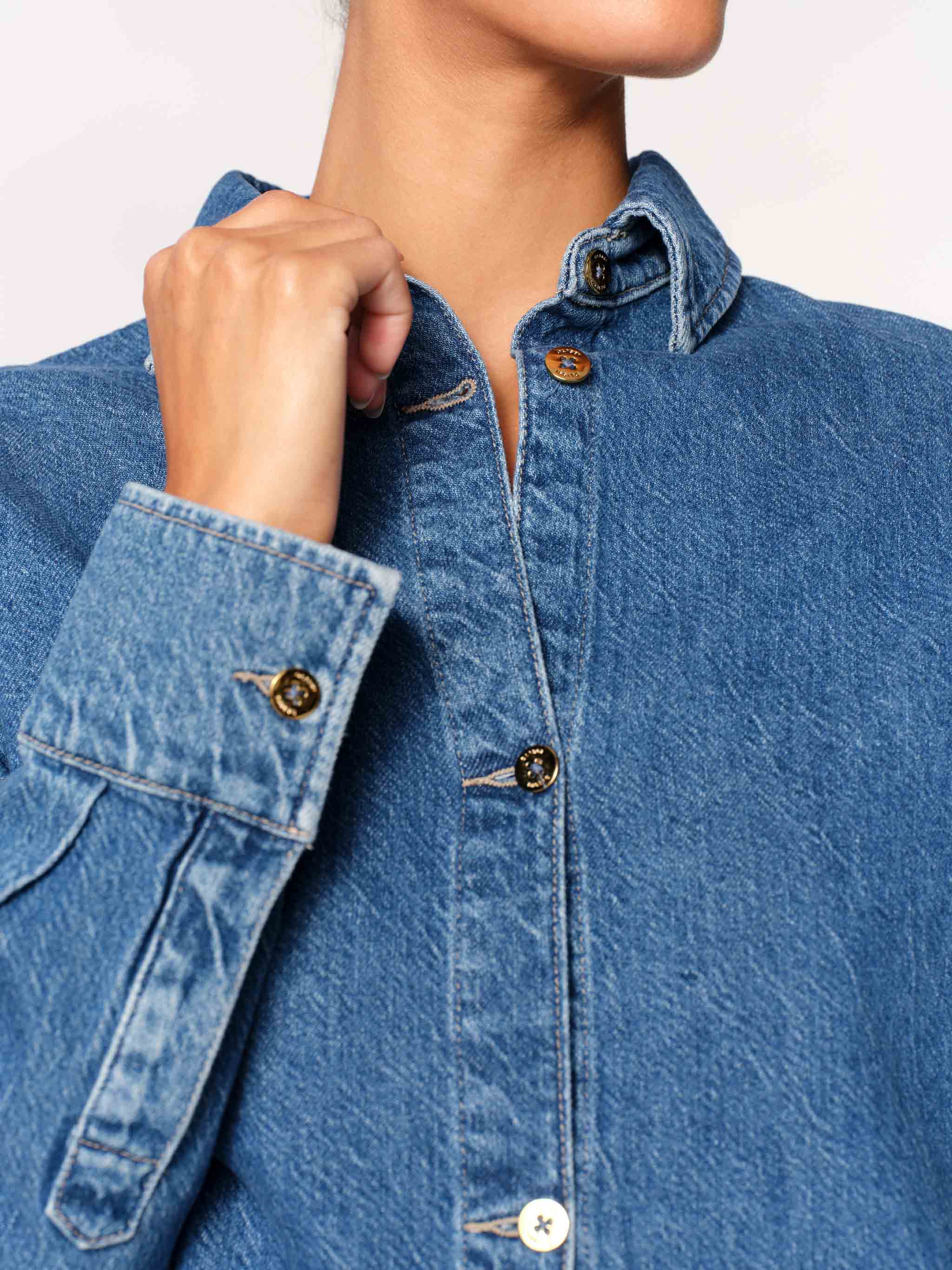 Close-up of a person wearing a blue denim shirt with buttoned sleeves.