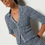 A model wearing a navy and white checkered smocked top with button closures and 3/4 sleeves.