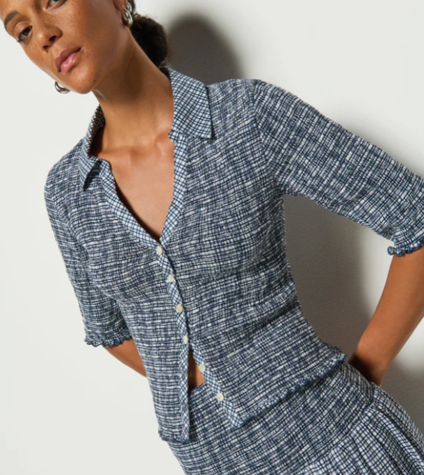 A model wearing a navy and white checkered smocked top with button closures and 3/4 sleeves.