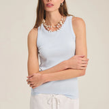 Woman wearing a light blue sleeveless top and white pants against a beige background