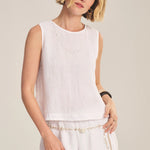 Woman wearing a white sleeveless top and pants against a plain background