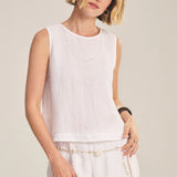 Woman wearing a white sleeveless top and pants against a plain background