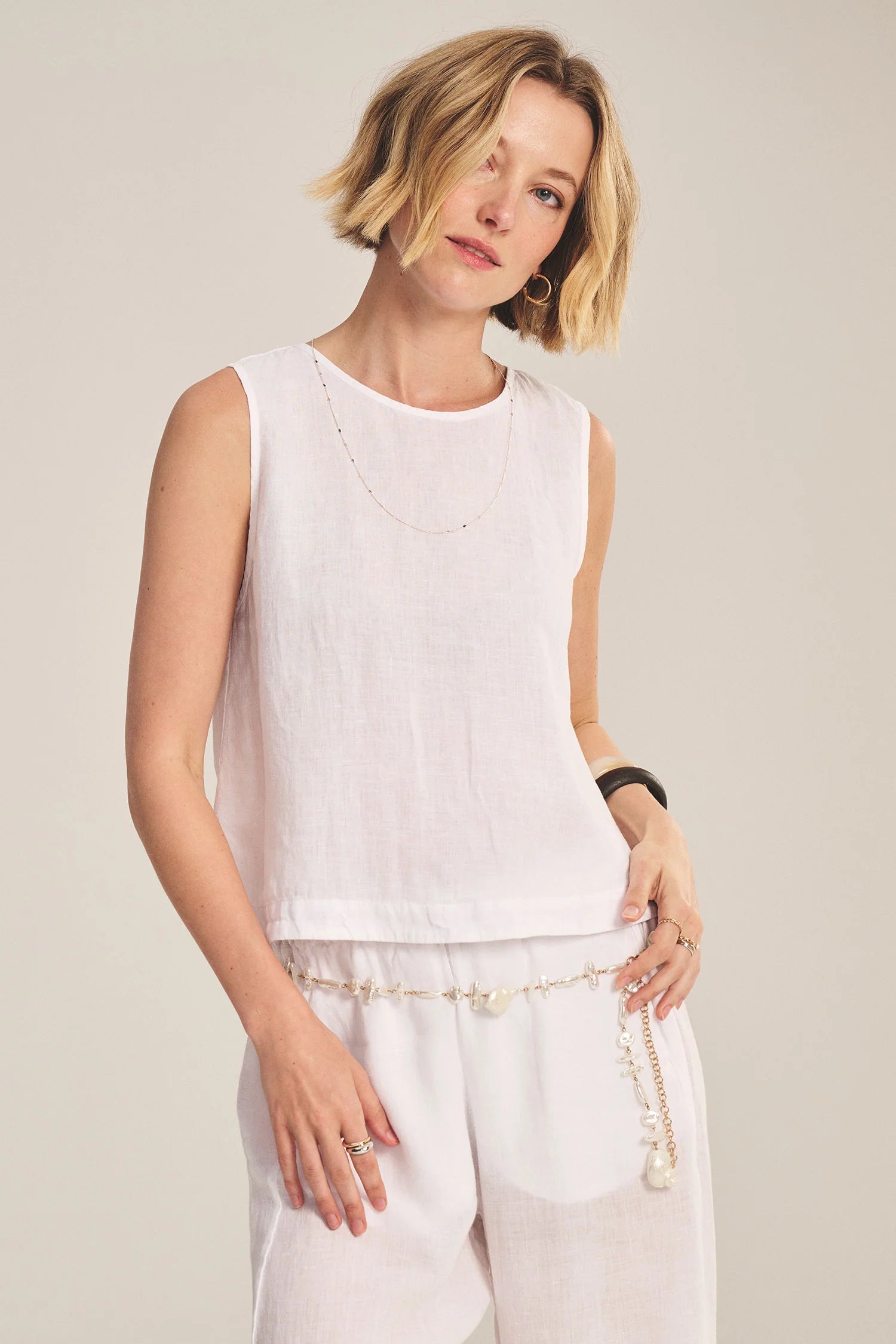 Woman wearing a white sleeveless top and pants against a plain background