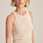 Woman wearing a beige and white striped sleeveless top against a plain background