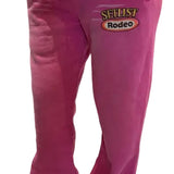Bright pink sweatpants with a drawstring waist and a 'SELLIST Rodeo' graphic on the left thigh, shown on a model wearing silver sneakers.