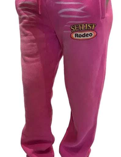 Bright pink sweatpants with a drawstring waist and a 'SELLIST Rodeo' graphic on the left thigh, shown on a model wearing silver sneakers.