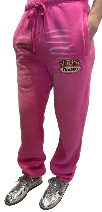 Bright pink sweatpants with a drawstring waist and a 'SELLIST Rodeo' graphic on the left thigh, shown on a model wearing silver sneakers.